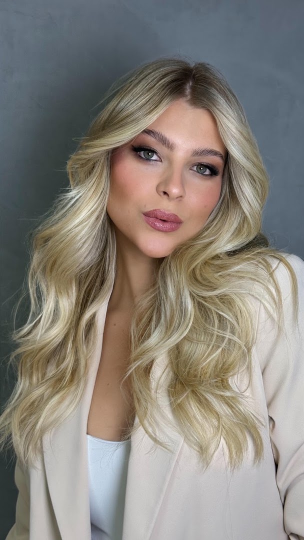Retrato de cliente loira com make natural e blazer bege, cabelo em ondas com mechas claras